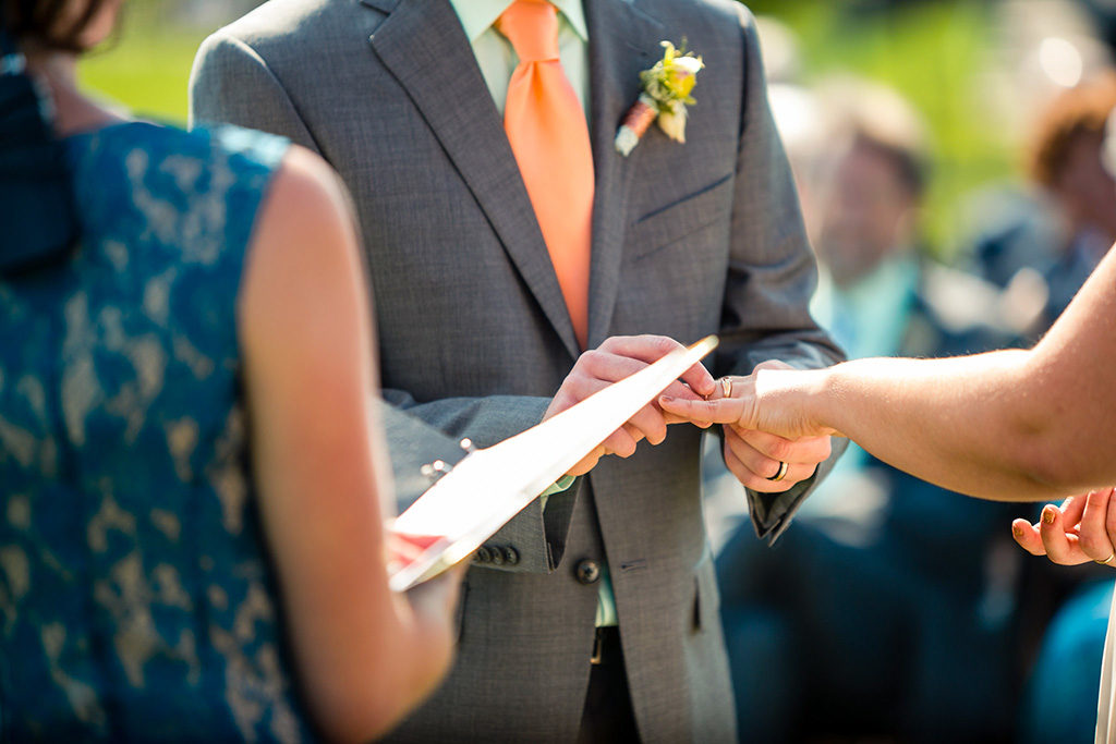 A woman officiating a wedding in Vermont while the groom puts a wedding ring on the bride's finger
