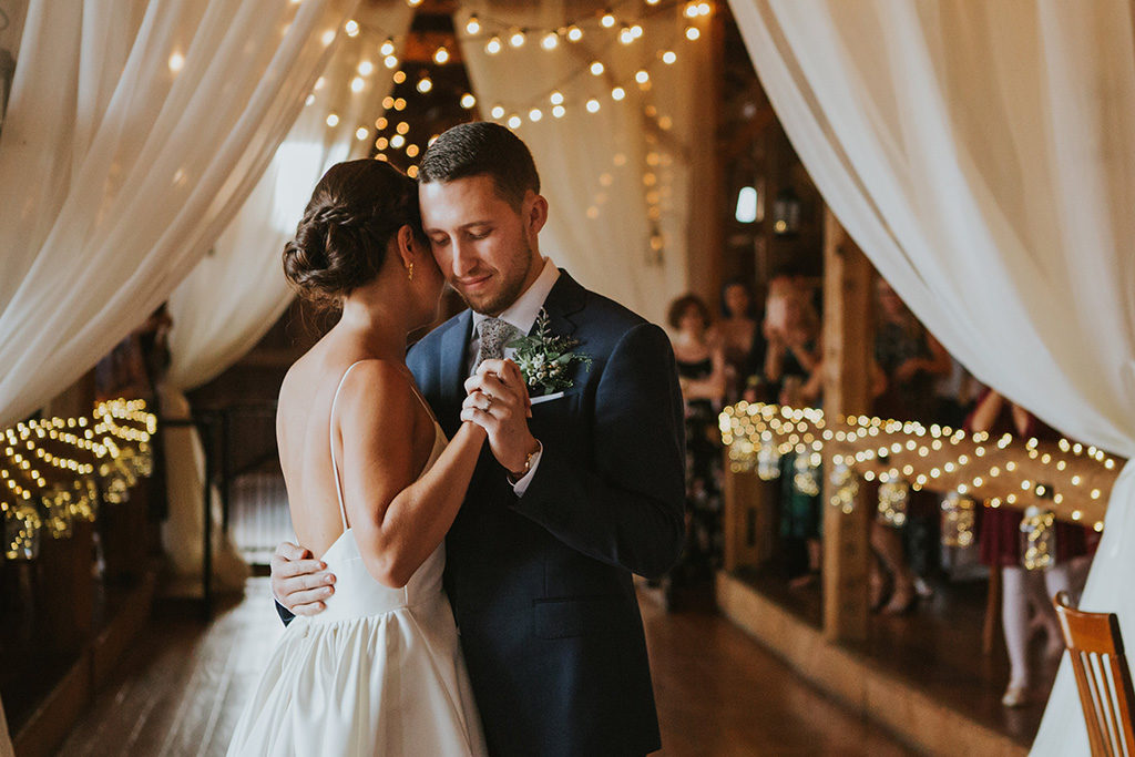 Newly married couple dancing together under string lights at their rustic Vermont wedding venue