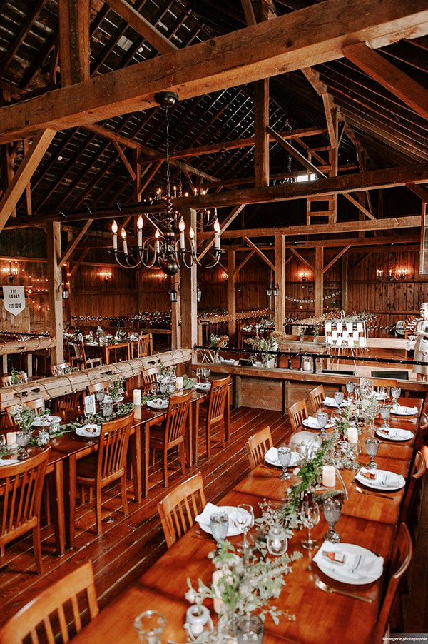 Interior of rustic barn venue, with wooden tables and chairs set for a wedding