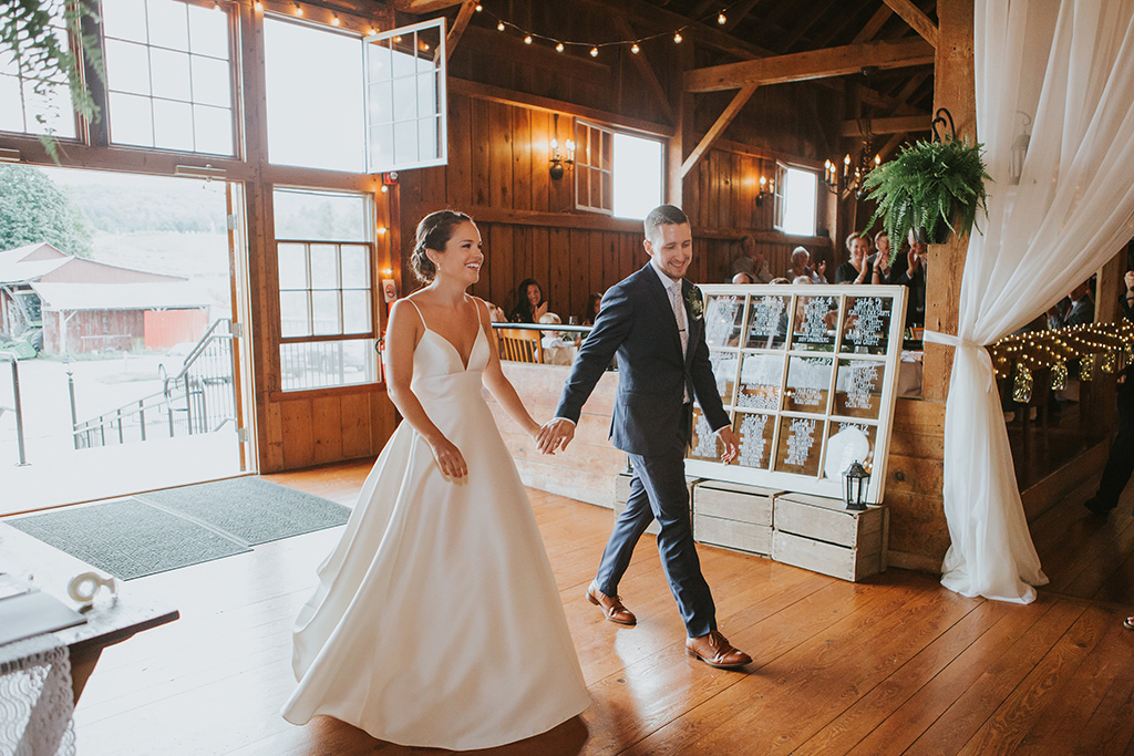 Newly married couple walking into a rustic wedding barn with string lights hanging overhead