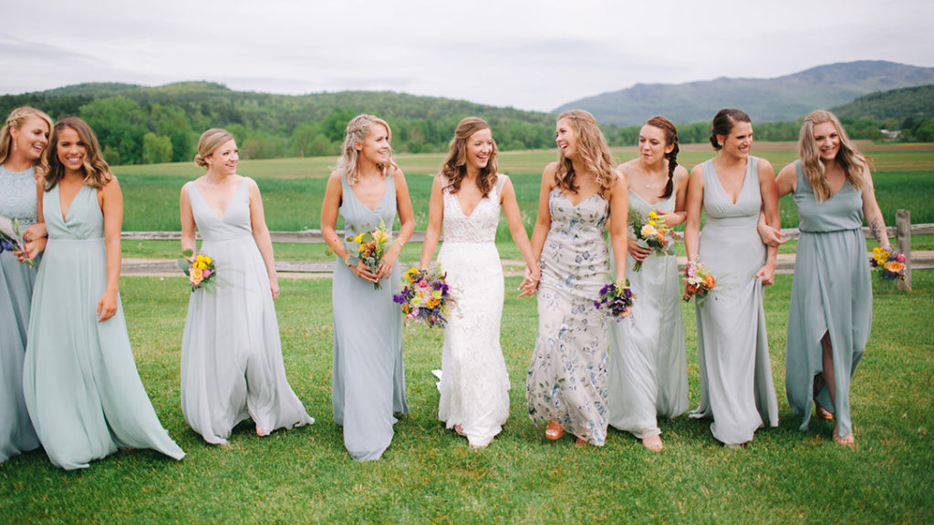 A bride and her bridesmaids walking together at her Vermont wedding venue with mountain views