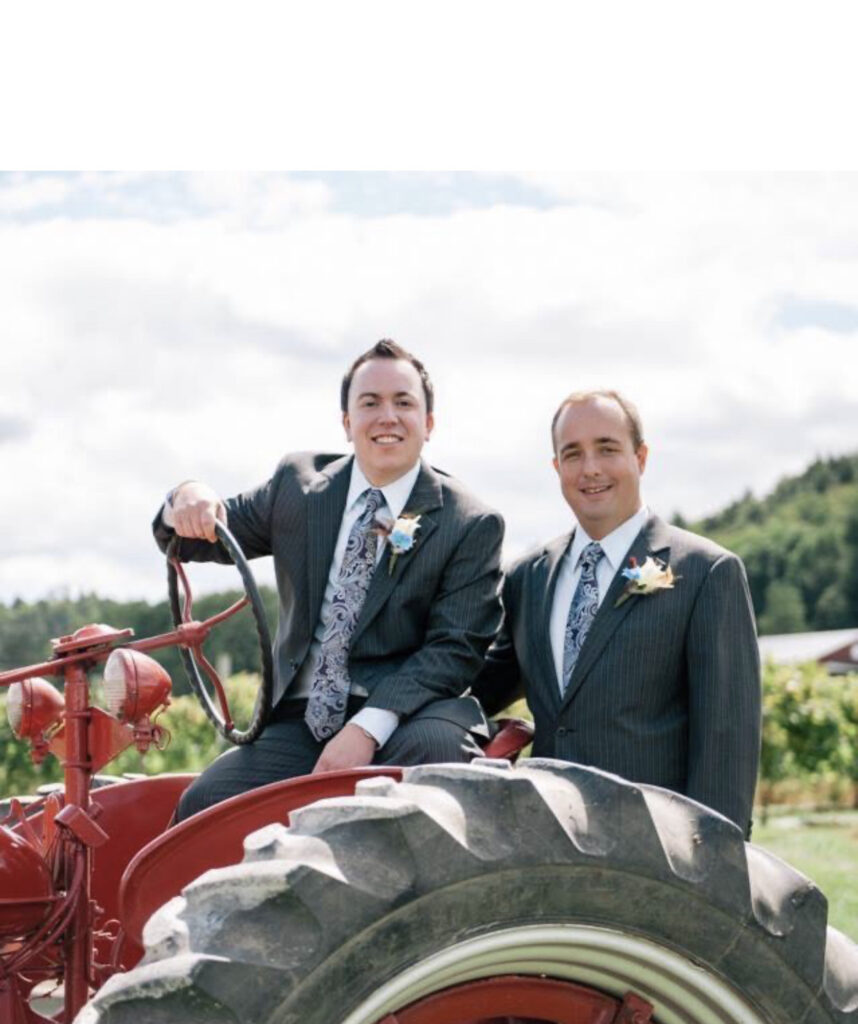 An LGBTQ+ couple posing together on a tractor at their rustic Vermont wedding venue