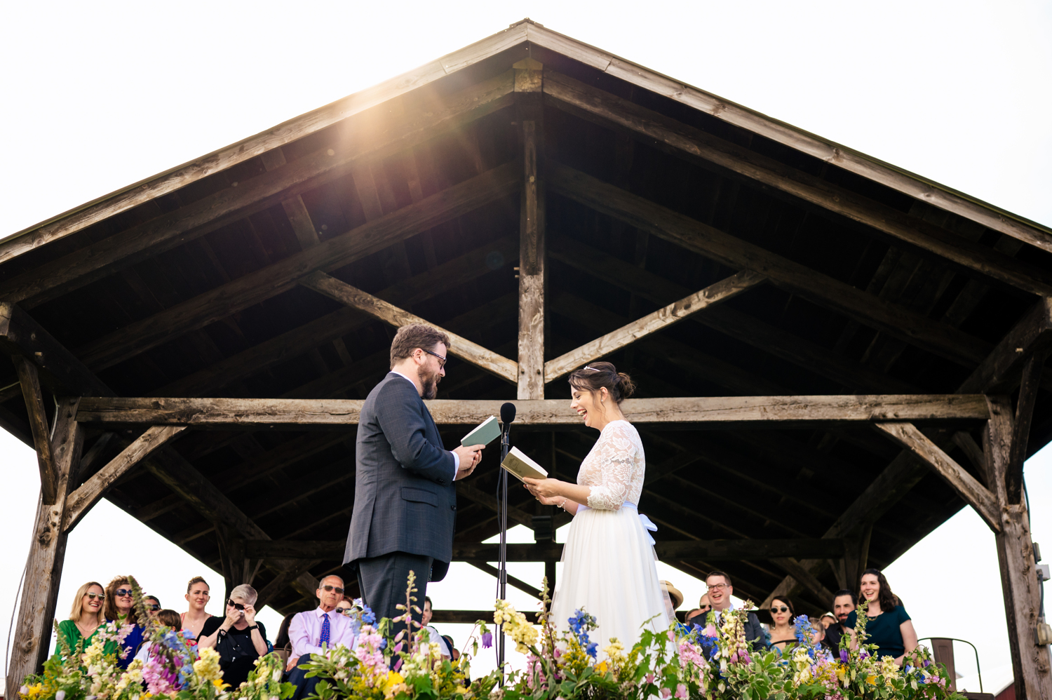 A couple laughing and exchanging their vows by a post and beam pavilion at their outdoor wedding in Vermont.
