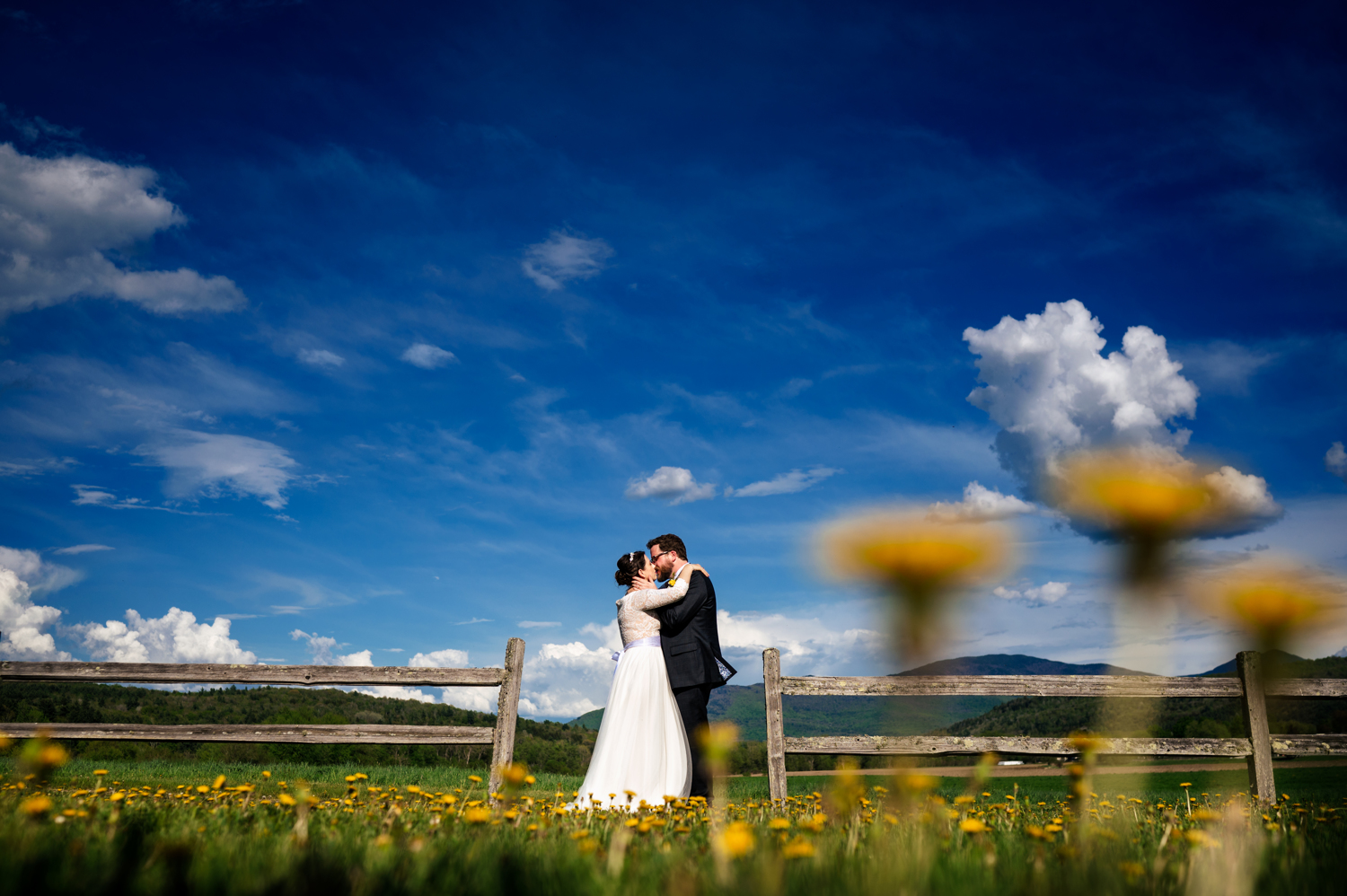 Anne and Jed standing together and kissing at their wedding venue with mountain views in Vermont