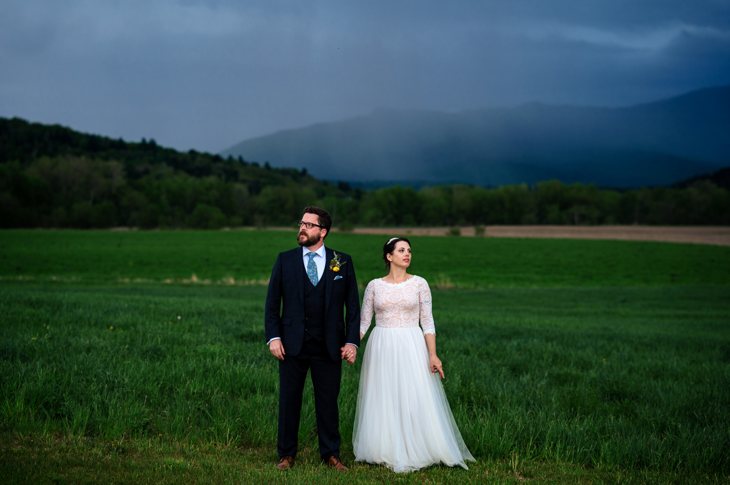 Anne and Jed standing together at their wedding venue with mountain views in Vermont while rain clouds gather behind them.