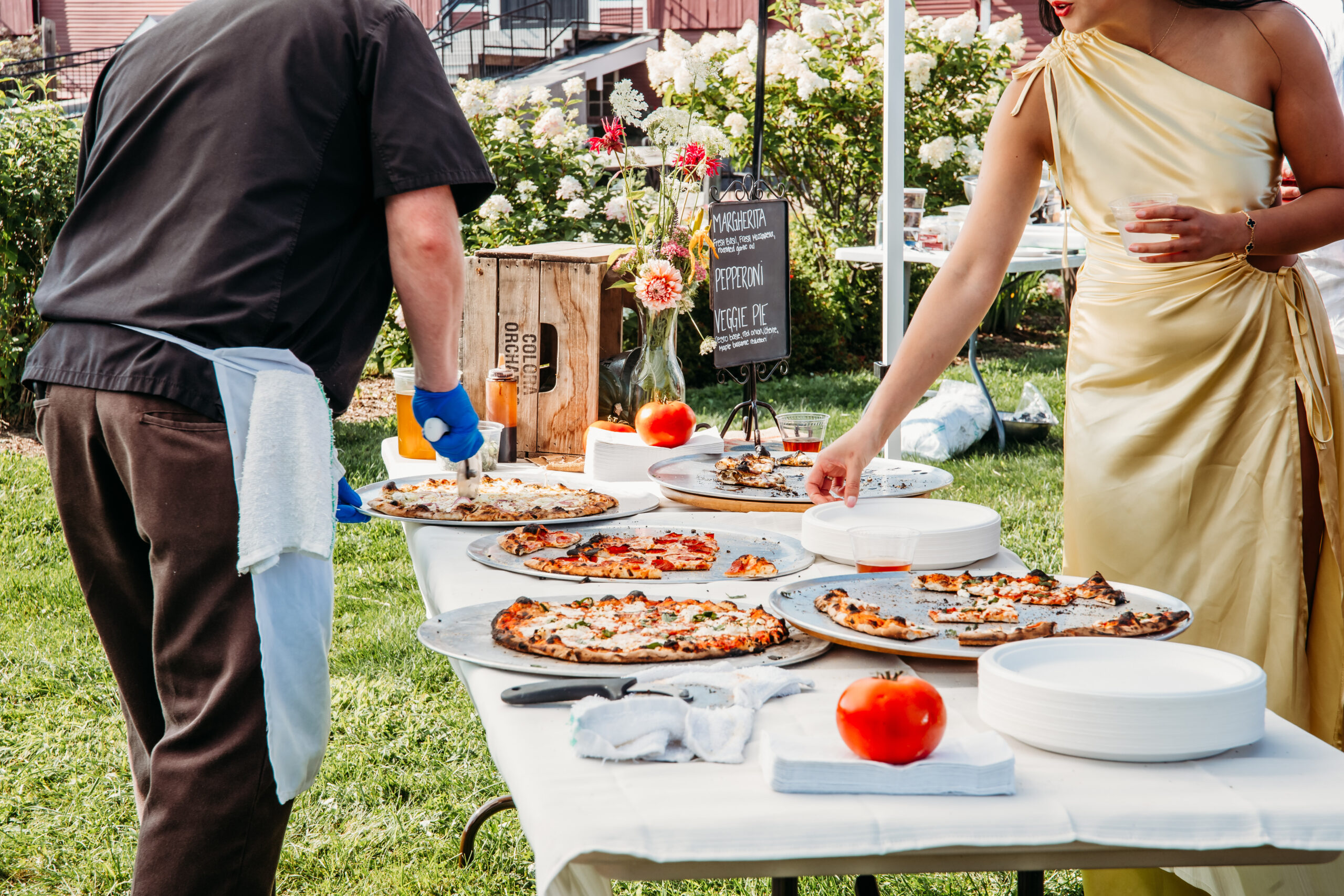 A vendor cutting up wood fired pizzas for a guest at a picnic wedding reception in Vermont.