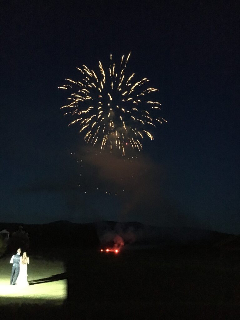 A couple standing underneath fireworks on the night of their summer wedding in Vermont.