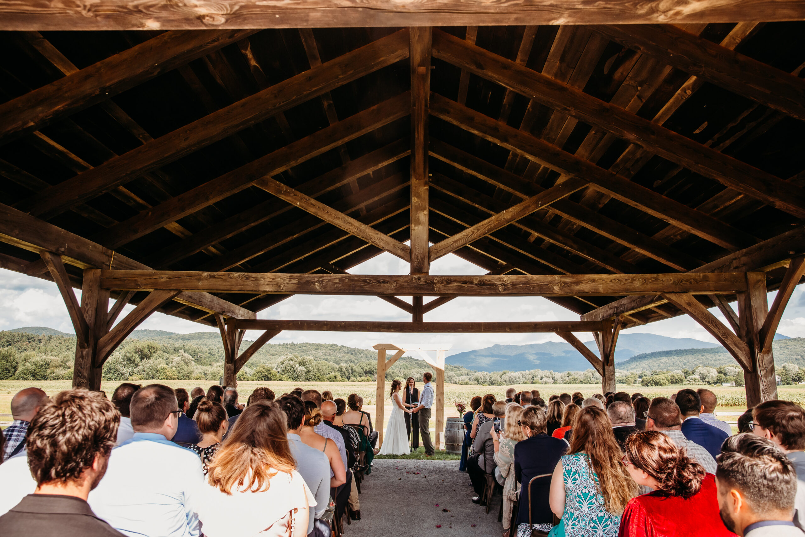 Jess and Greg standing together in front of their handmade wedding arbor at their farmers market themed wedding in Vermont