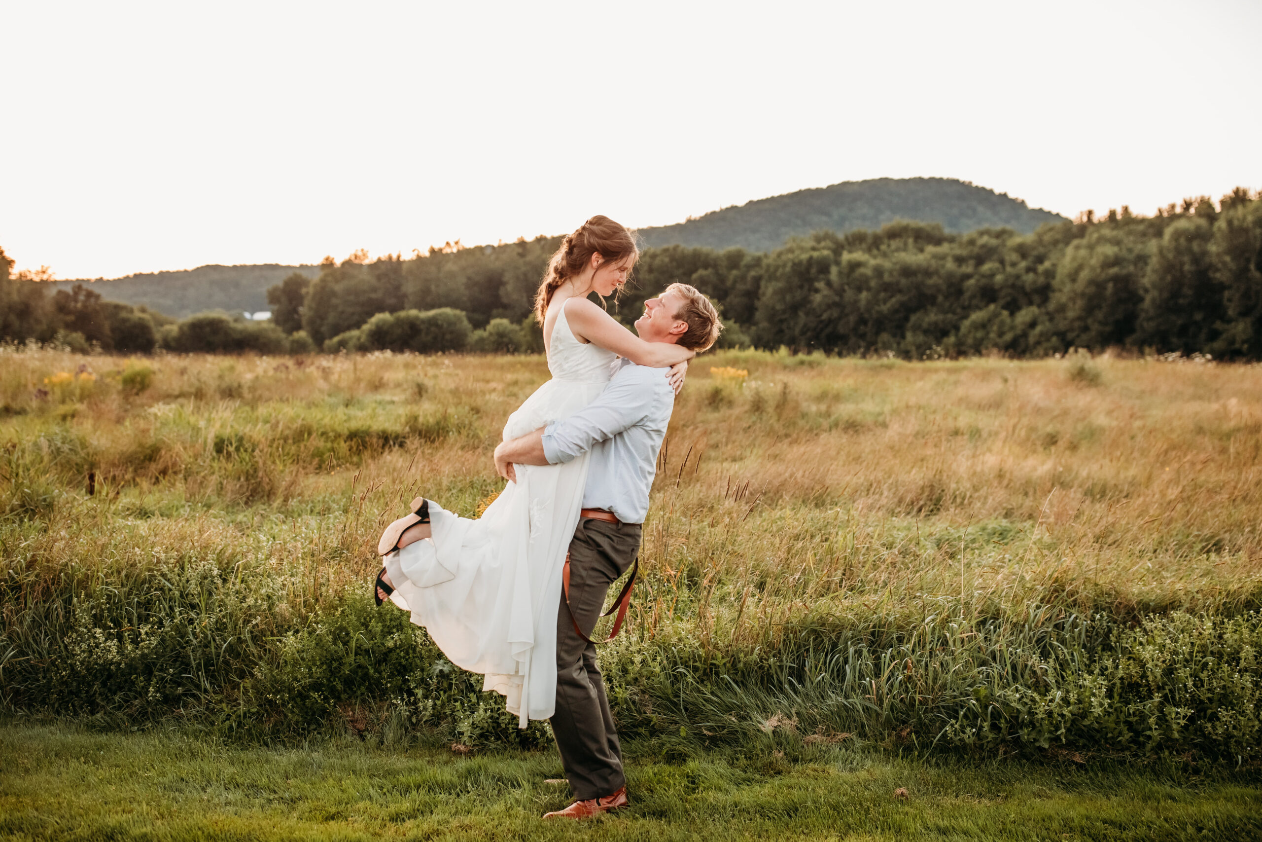 Greg holding Jess in his arms outside in a field at their Vermont farm wedding venue