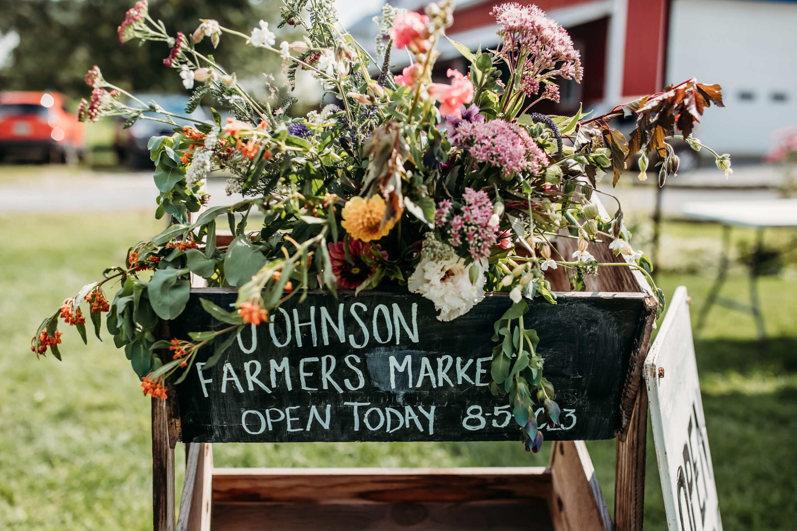 A wooden cart of flowers and chalkboard sign at Jess and Greg's farmers market themed wedding reception in Vermont
