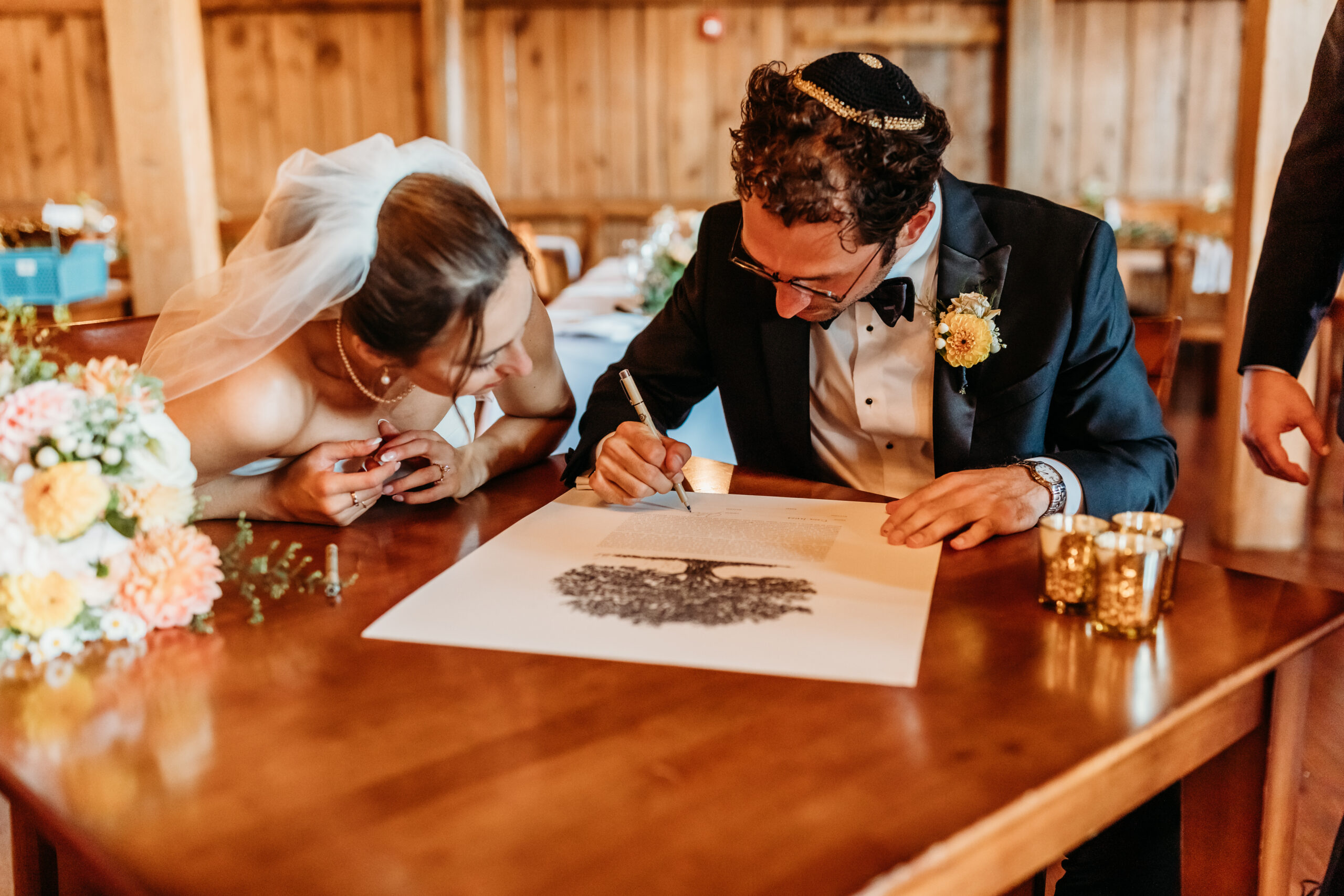 The groom signing the ketubah next to his wife