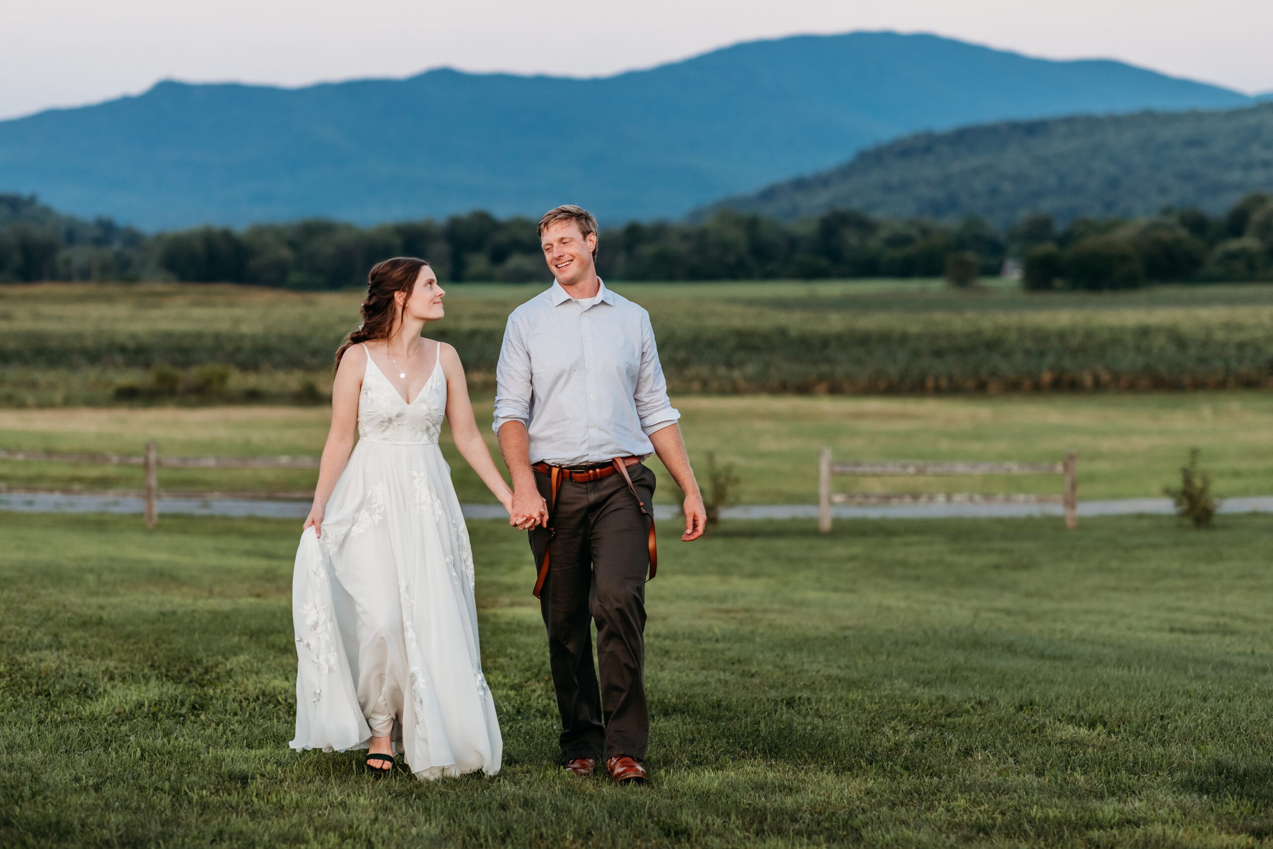 Jess and Greg holding hands and walking together outside at their Vermont farm wedding venue with mountains views