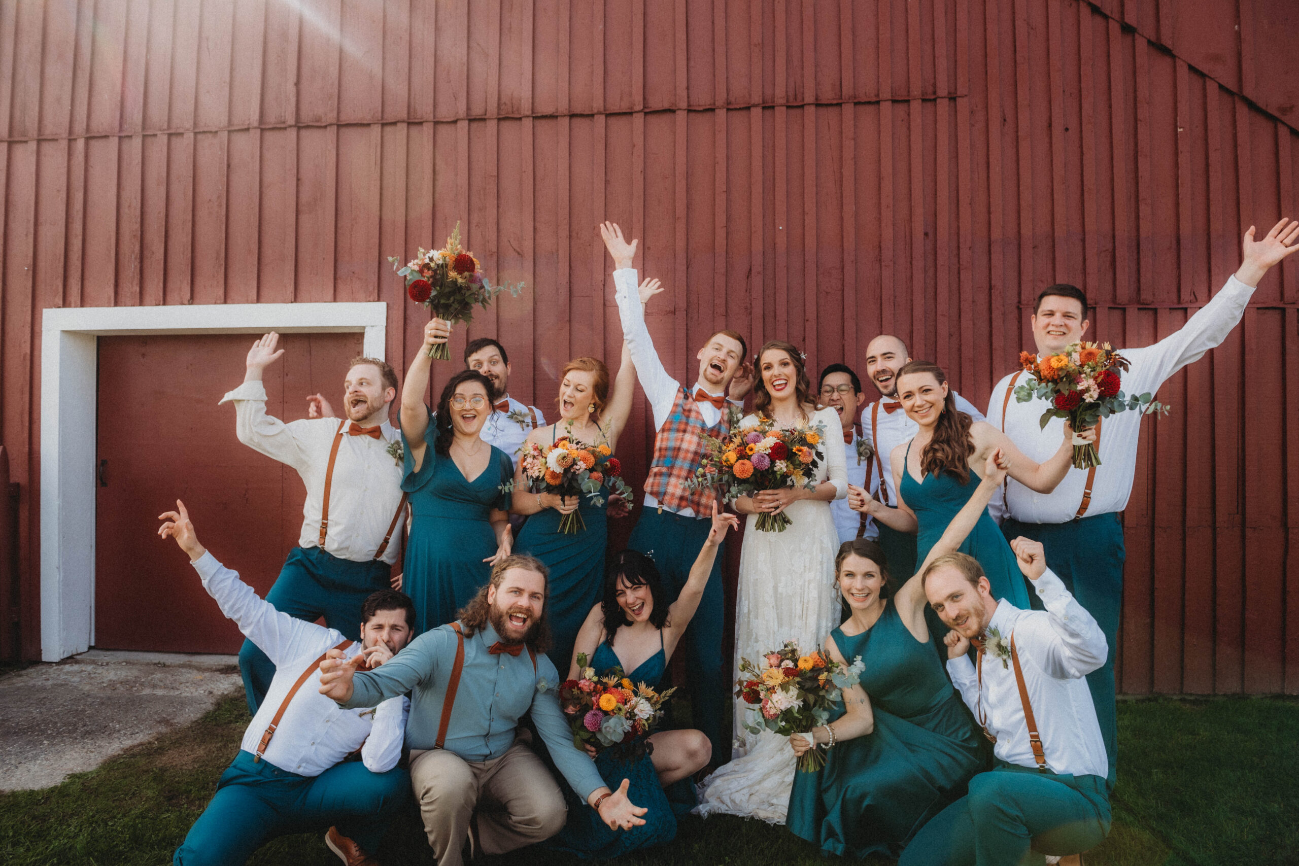 The wedding party standing and kneeling together for a group photo outside of the rustic wedding barn