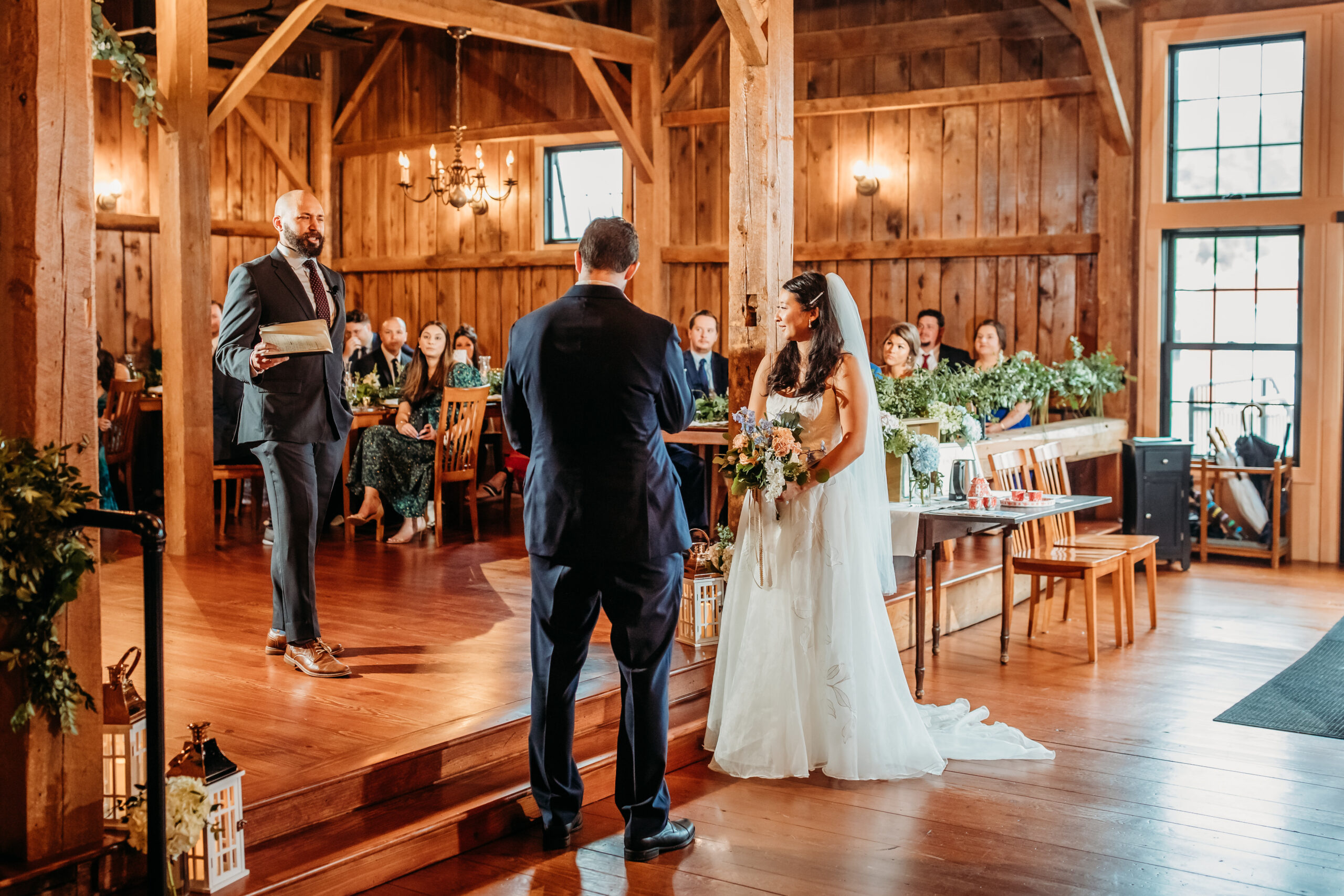A bride and groom being married by a man while guests watch inside The Barn at Boyden Farm's rustic barn venue