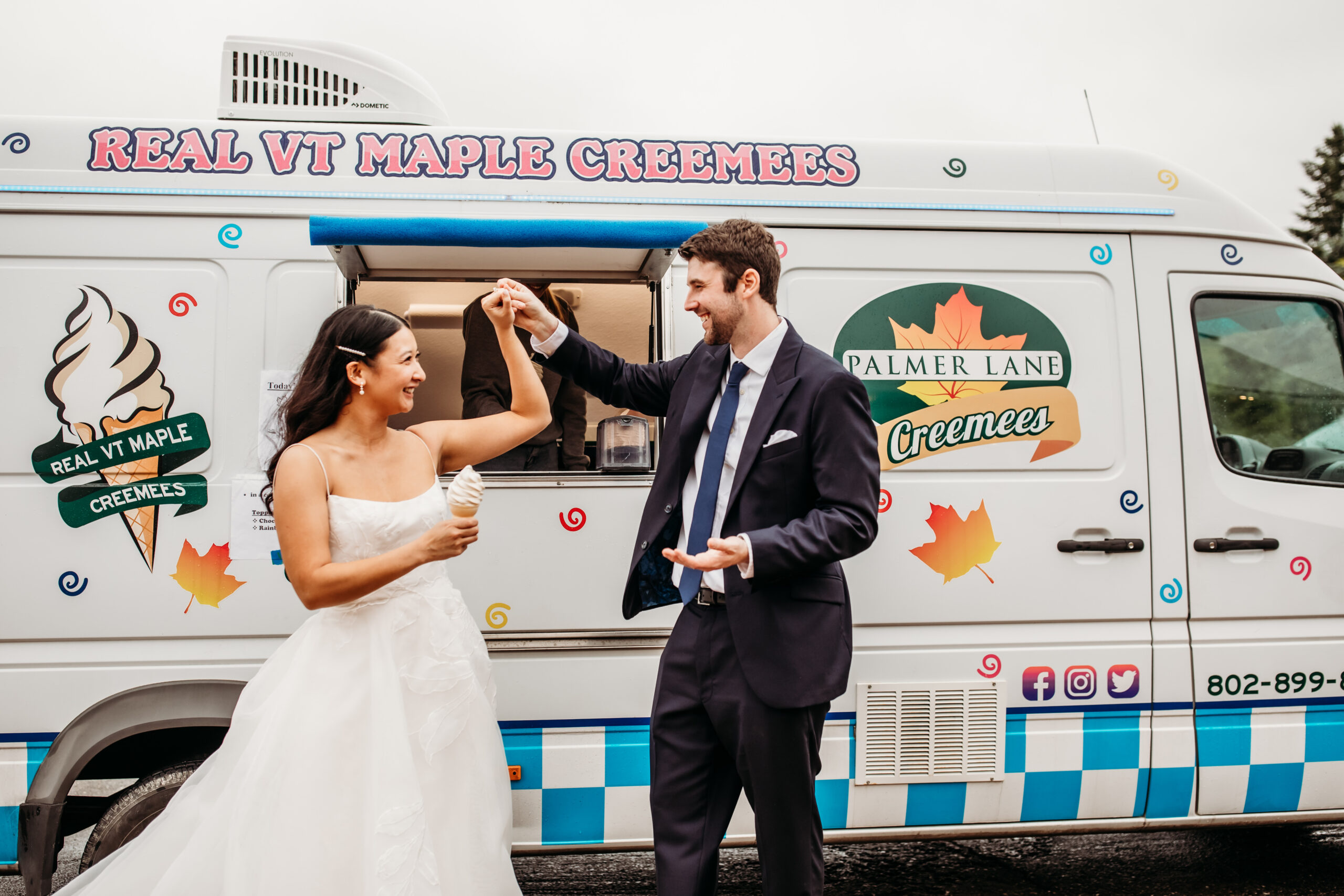 A bride and a groom holding maple creemees and dancing together in front of a creemee truck at their summer barn wedding in Vermont