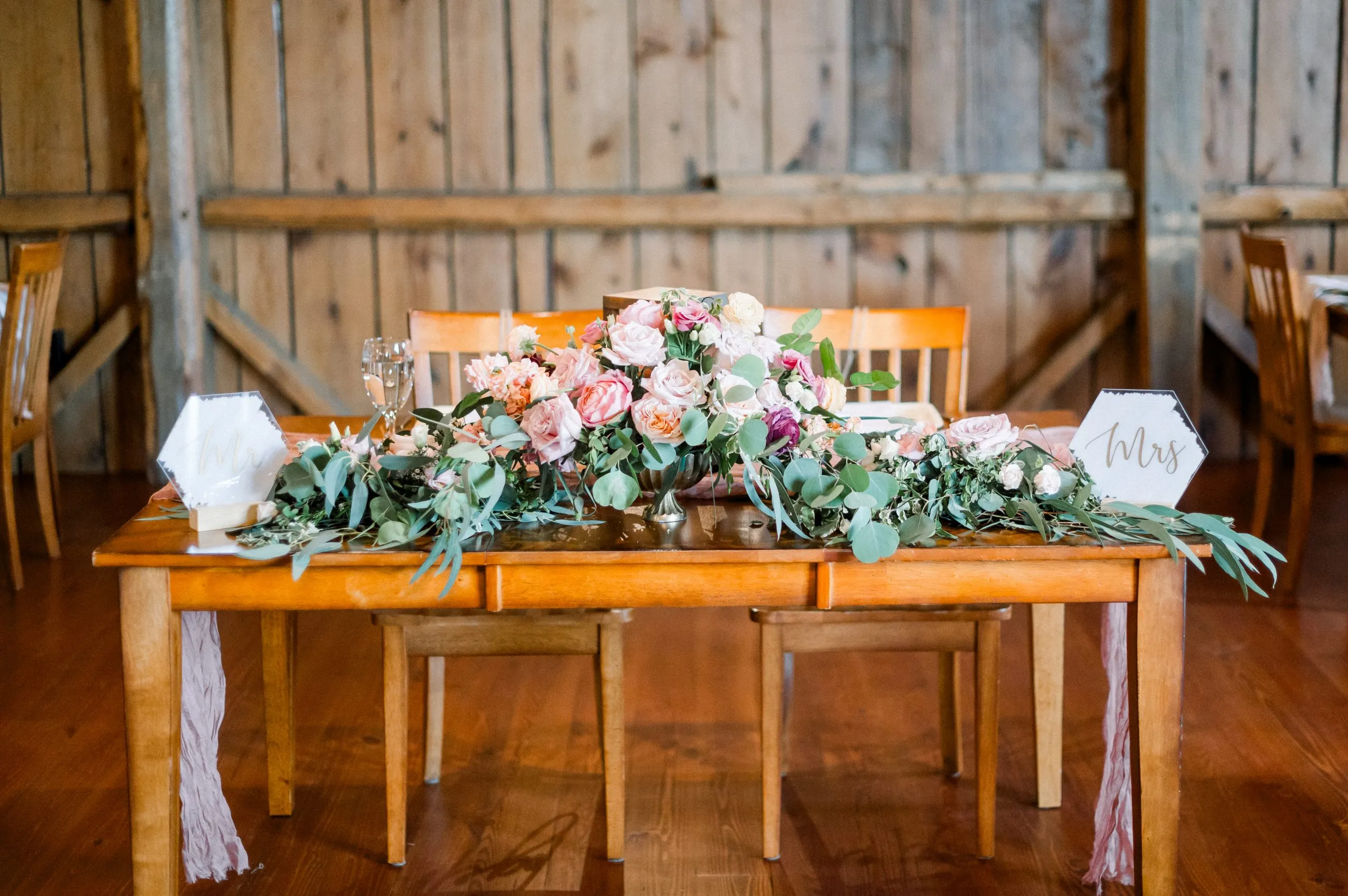 A large floral arrangement with greenery on a table inside a rustic barn at a garden party themed wedding