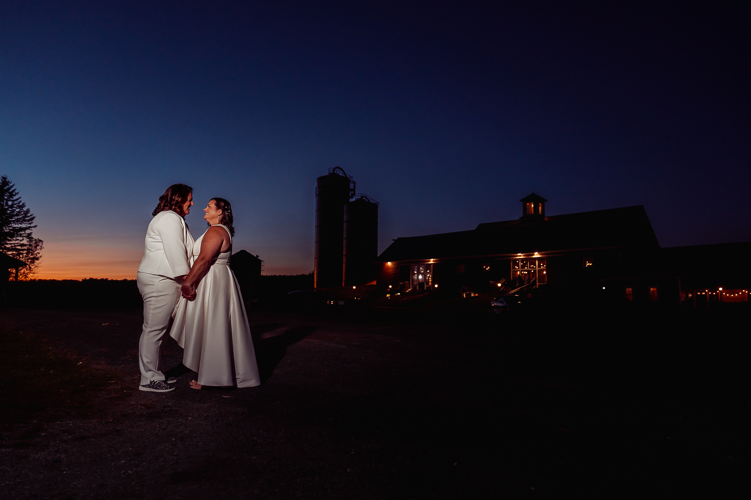 Darlene and Denise standing together outside in the dark with the wedding barn and a sunset in the background