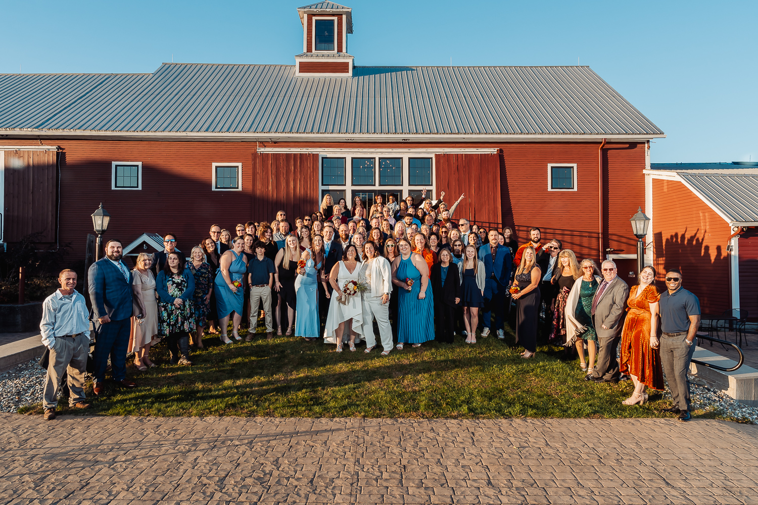 Darlene and Denise's wedding guests gathered for a picture at their outdoor October wedding with the rustic barn behind them