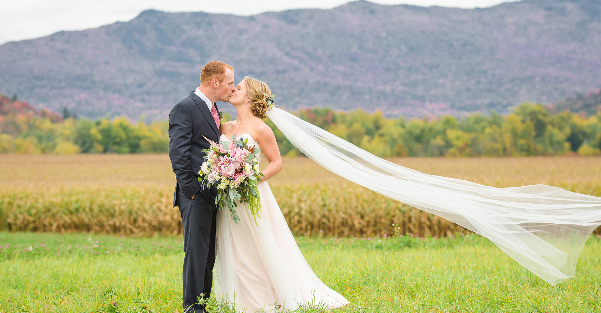 Bride and groom kissing at their Vermont wedding venue with fall foliage and mountains in the background.